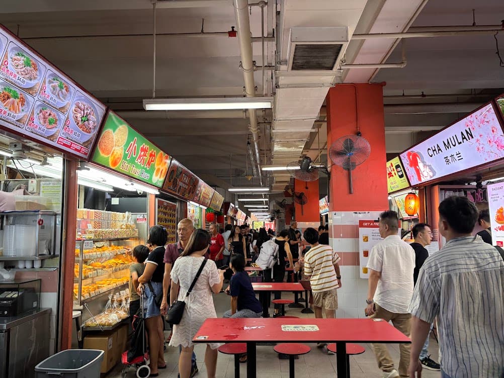 Busy hawker centre in Chinatown, Singapore, with diners at red tables and food stalls in the background