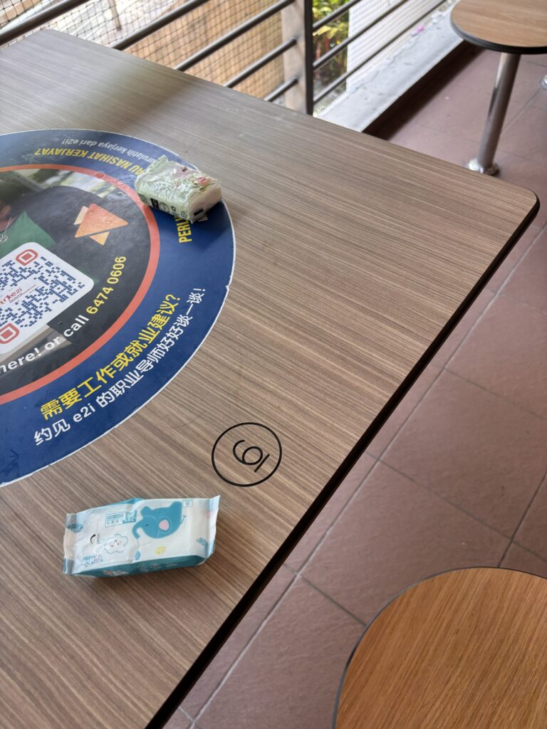 Close-up of a Singapore hawker centre table, showing a tissue packet and baby wipes placed to 'chope' or reserve the seat.