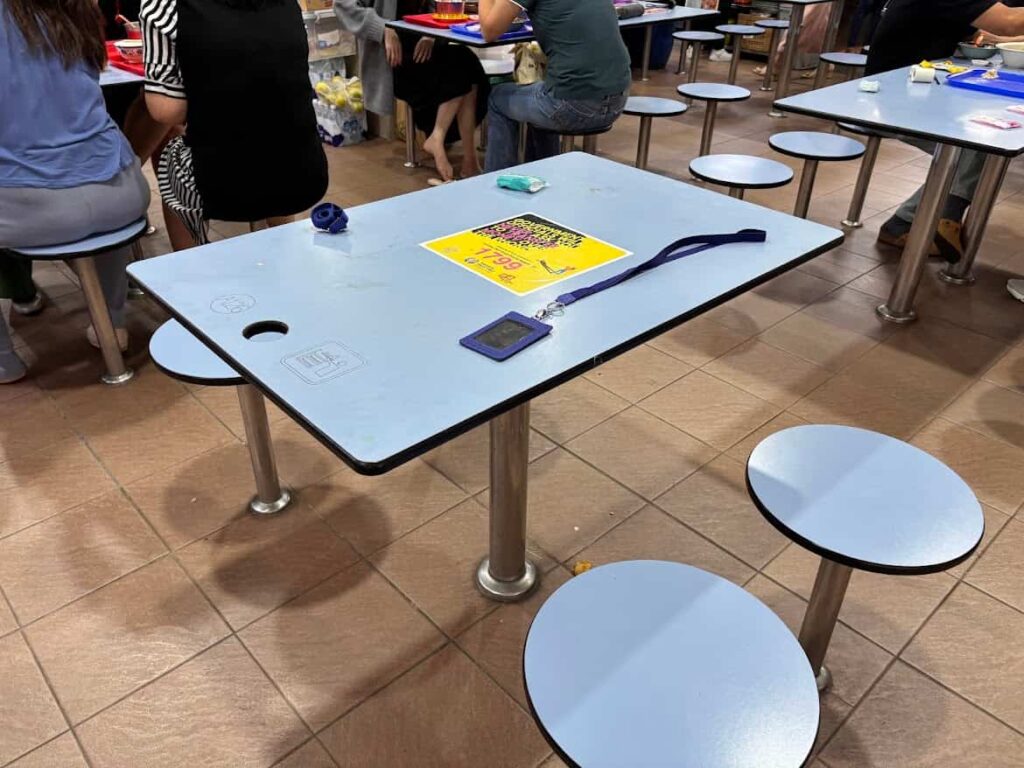 A table at a Singapore hawker centre with a lanyard, ID card and tissue packet placed on it to "chope" or reserve the seat while the diners order food.