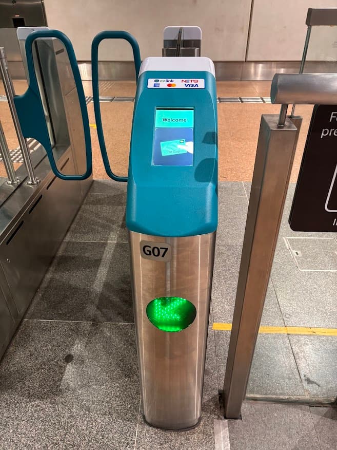 A Singapore MRT fare gantry with a green arrow indicating an active lane for passengers to tap in or out.