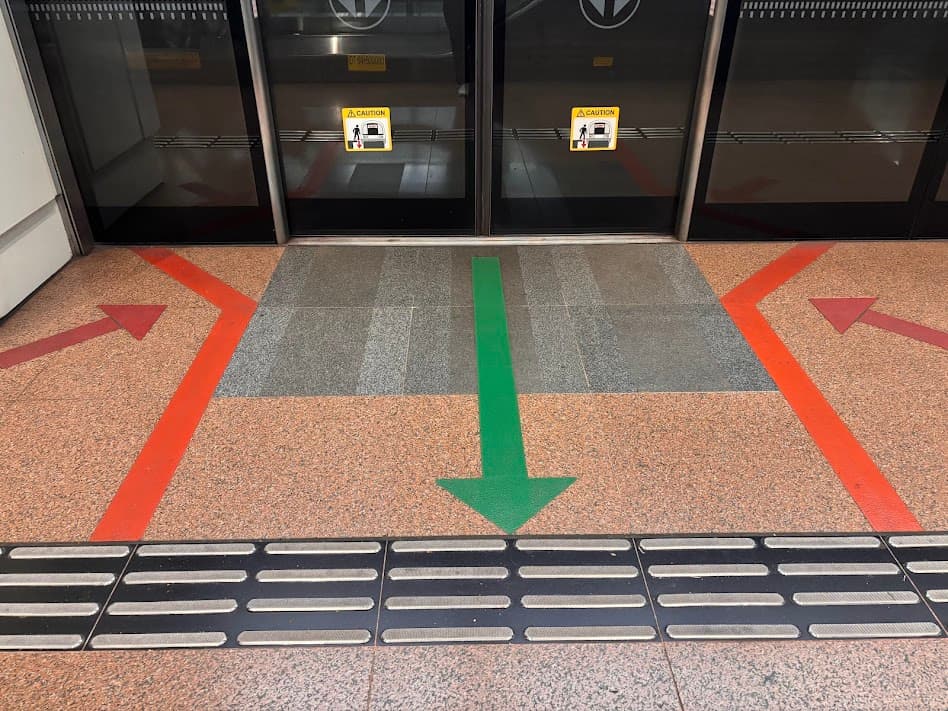 Floor markings at a Singapore MRT station showing red arrows for boarding on the sides and a green arrow for exiting in the middle.