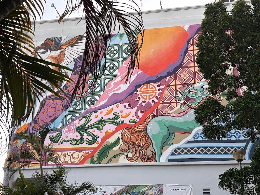 A large, colorful outdoor wall mural featuring a bird, a stylized mythical creature, and traditional patterns.