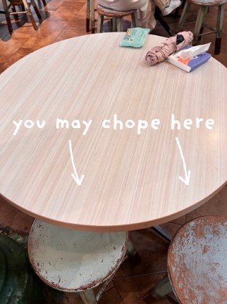 A round table in a crowded hawker centre with a umbrella and tissue packs occupying one side, illustrating how to 'chope' half of an unoccupied table