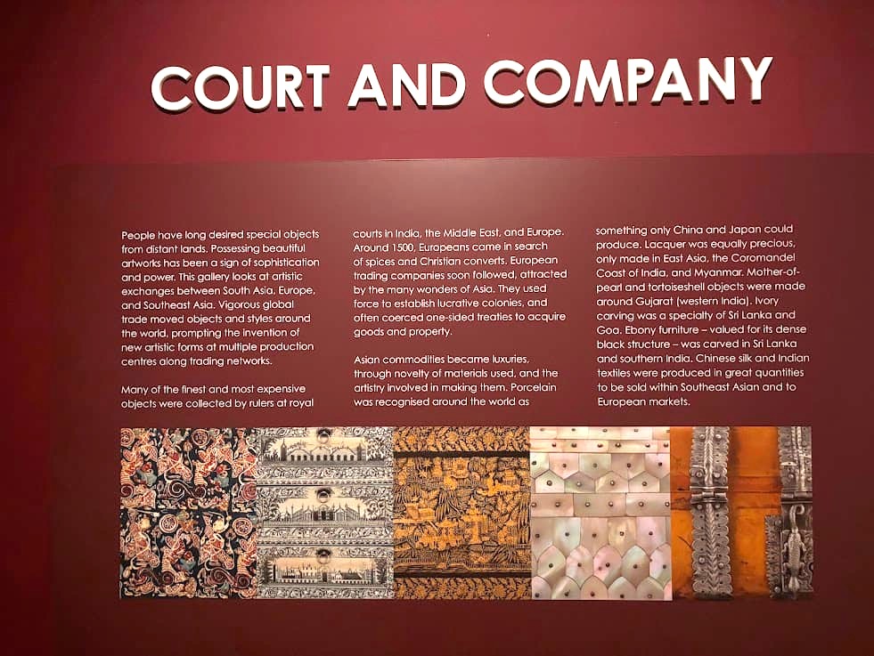 A museum wall display at the Asian Civilisations Museum Singapore titled "Court and Company" with text panels and decorative textile or art panels in rich red, gold, and brown tones.