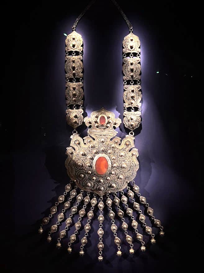 A large ornate amulet necklace from 19th-century Bukhara, Uzbekistan, made of gilded silver with turquoise, coral, and agate gemstones, displayed at the Asian Civilisations Museum Singapore