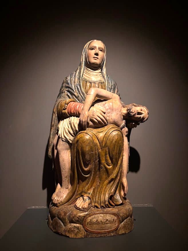 A carved and painted Pietà sculpture depicting the Virgin Mary cradling the body of Jesus, on display at the Asian Civilisations Museum Singapore.