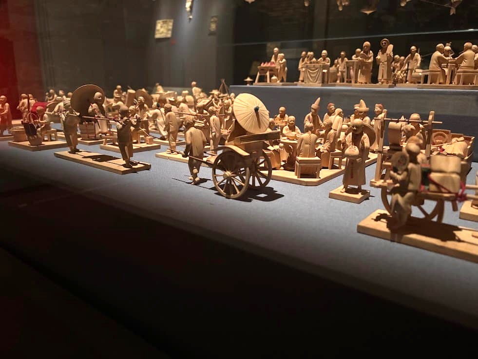 A wide-angle display of 109 boxwood figurines from 1930s Shanghai showing a bustling street procession with carts, horses, and crowds, at the Asian Civilisations Museum Singapore.