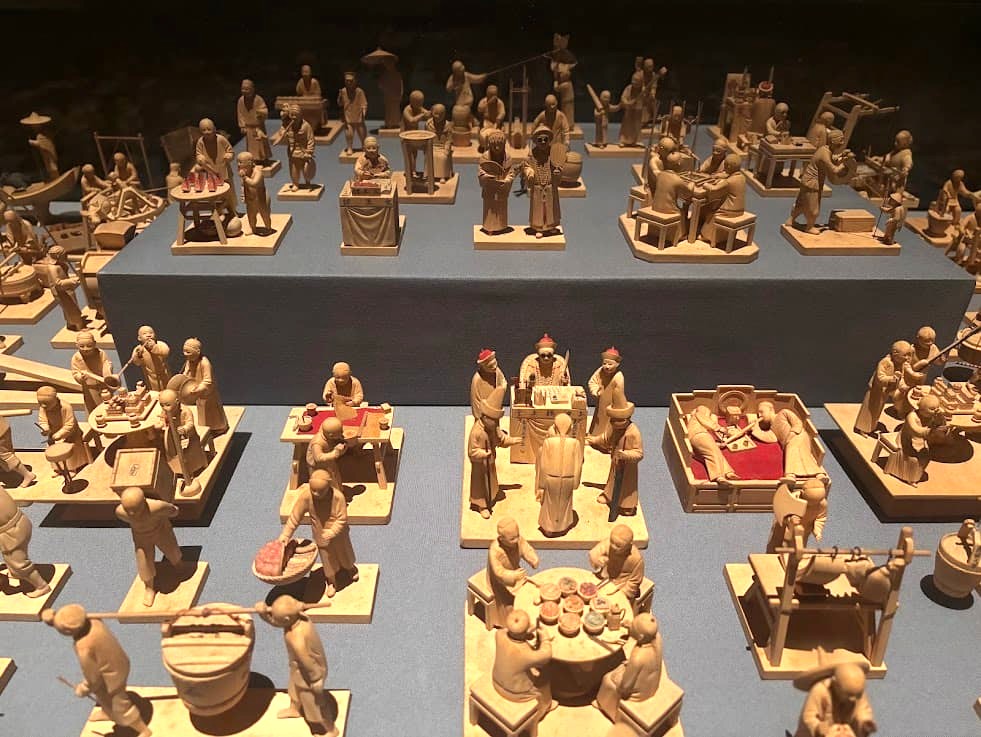 A close-up display of 109 boxwood figurines from 1930s Shanghai depicting scenes of Chinese daily life including merchants, diners, and court officials, at the Asian Civilisations Museum Singapore.