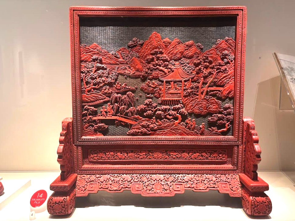 A richly carved red lacquered wood table screen depicting the Gathering at the Orchid Pavilion, on display at the Asian Civilisations Museum Singapore.