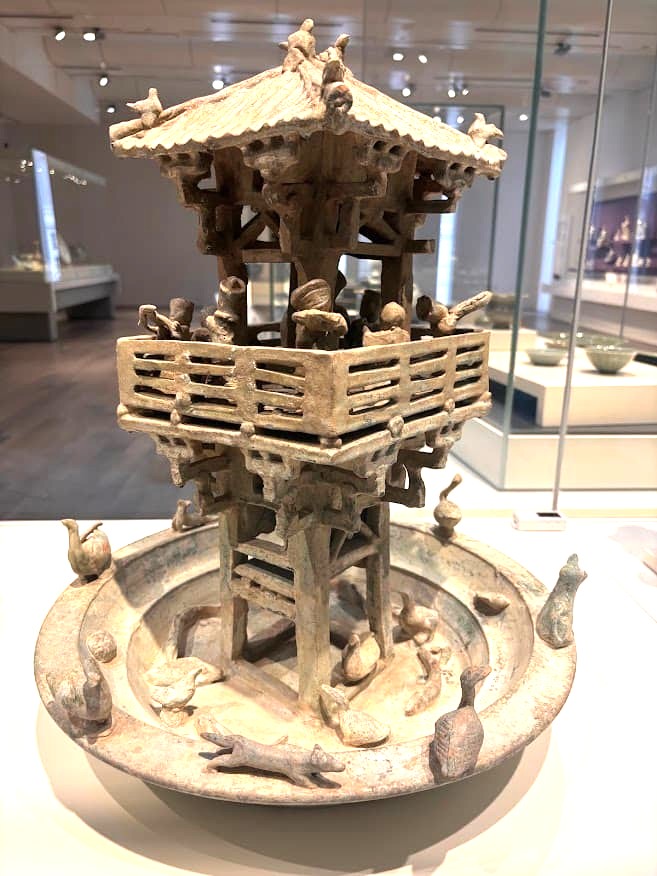 A Han dynasty earthenware model of a multistorey tower with a moat, decorated with figures of dancers, musicians, and animals, on display at the Asian Civilisations Museum Singapore.