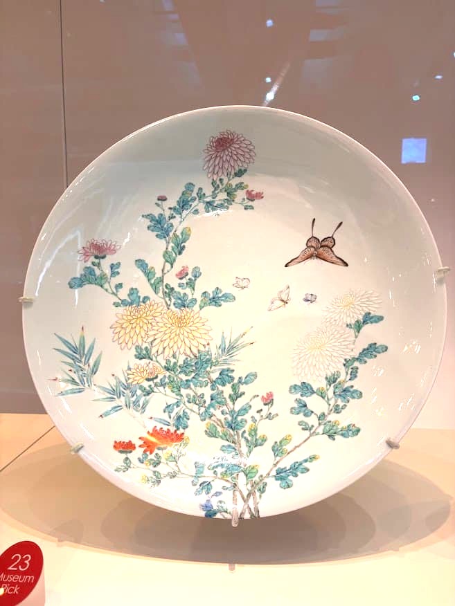 A large Chinese porcelain dish decorated with delicate chrysanthemum flowers, birds, and foliage in soft pastel colours, on display at the Asian Civilisations Museum Singapore.