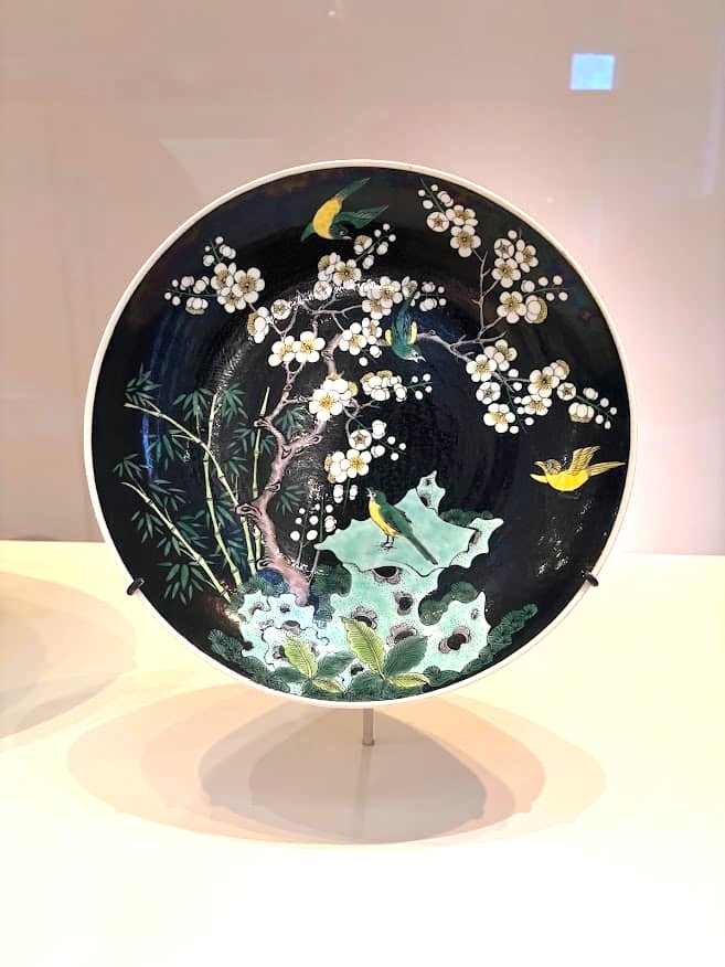 A large black-glazed porcelain dish decorated with colourful birds, blossoming prunus branches, pine, and bamboo — the Three Friends of Winter motif — on display at the Asian Civilisations Museum Singapore.